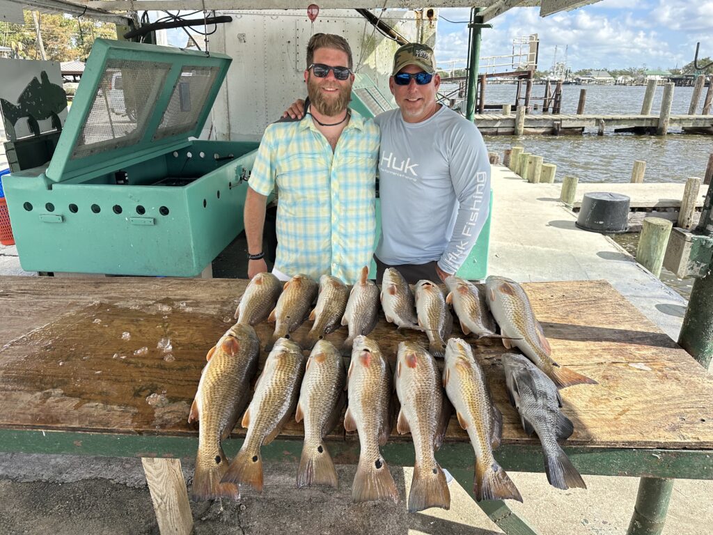 Two men standing in front of the red fish they caught on their New Orleans fishing charter